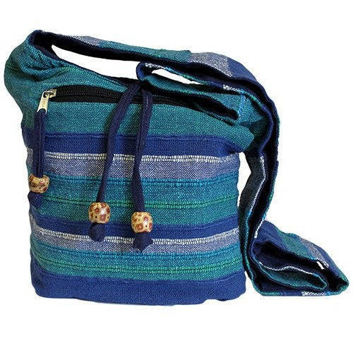 A fabric shoulder bag rests on a white surface. It has blue and green horizontal stripes, a black zipper and blue drawstrings with decorative wooden beads.