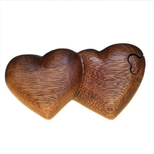 Two interlocking wooden hearts lie side by side, intricately carved with a smooth finish. The context is a plain, white background that emphasizes the detailed texture.