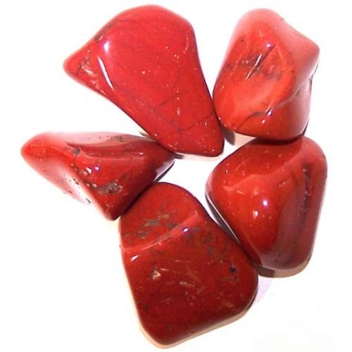 Red, tumbled gemstones sit together on a white surface, appearing polished and irregularly shaped.