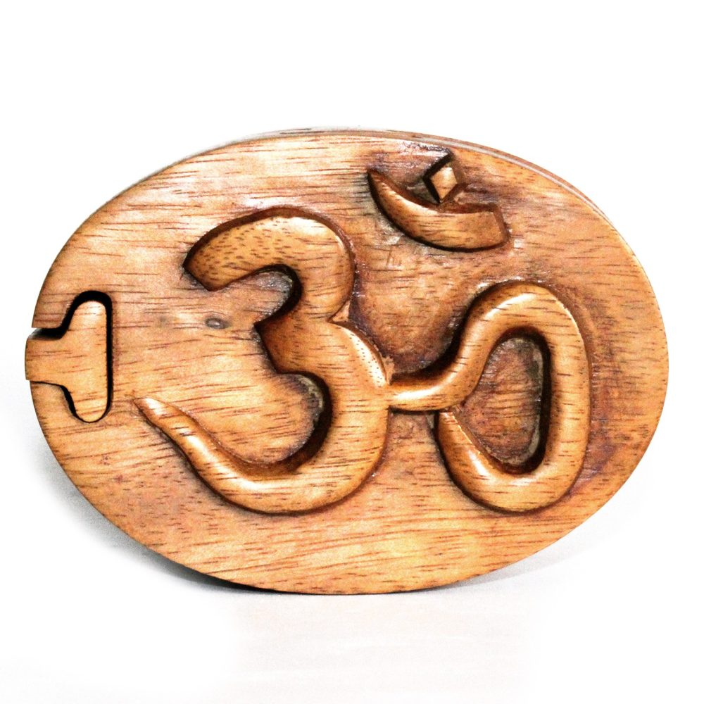 A wooden box features an intricate carving of the symbol "ॐ" on its lid, with each piece forming part of the design. The box sits on a white background.