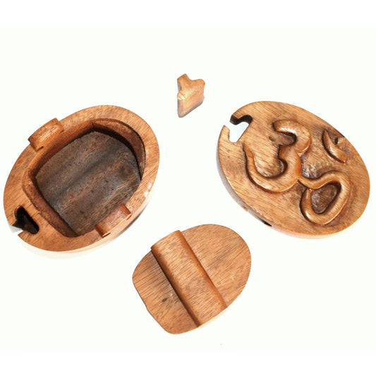 A disassembled wooden puzzle box with pieces arranged separately, featuring intricate carved designs including the "Om" symbol on one piece. The light wooden context highlights the craftsmanship.