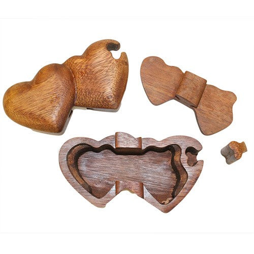 Wooden heart-shaped puzzle box disassembled on a white background. The main heart piece is separated into two parts with a small key component. The interior shows a hollow compartment.