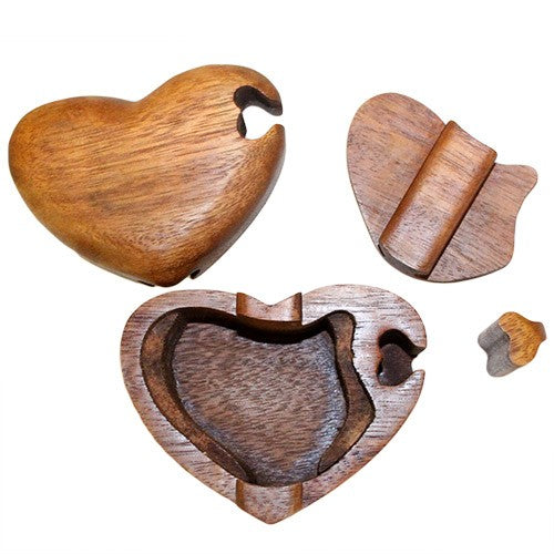 A wooden, heart-shaped puzzle box is disassembled, showing its separate lid and two internal pieces. The smooth wooden finish highlights intricate craftsmanship, revealing hidden compartments on a white background.