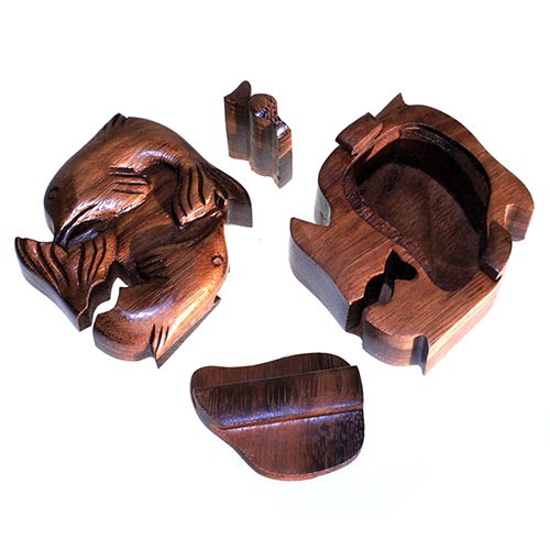 Wooden puzzle box pieces shaped like a fish are disassembled and scattered. The lid and compartment are visible, resting on a white surface.