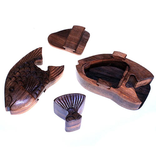 A wooden fish puzzle box, disassembled into four pieces, lies on a white surface. The main body and three detachable parts, including the tail and head, reveal storage space inside.
