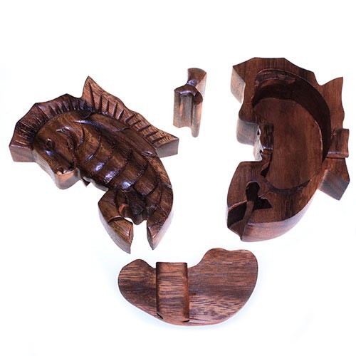 Wooden seahorse puzzle box, disassembled into several pieces, resting on a white surface. The box features intricate carving and dark wood tones, with parts including the seahorse lid and internal locking mechanisms.