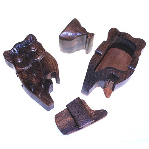 A wooden owl puzzle box disassembled into four pieces, revealing its carved structure and hollow interior, with pieces arranged on a flat, light-colored surface.