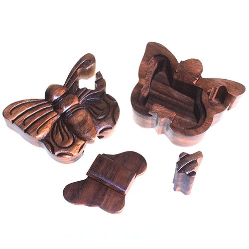 A wooden butterfly-shaped puzzle box, disassembled into four pieces, rests on a white surface. The pieces include the butterfly's top, bottom, and two internal components.