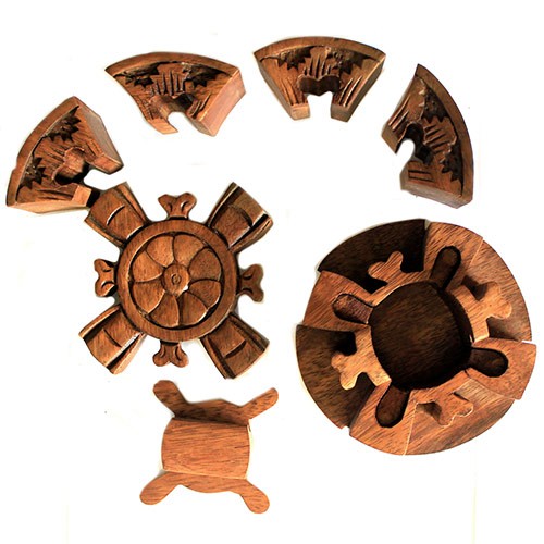 Wooden puzzle pieces scattered, featuring interlocking segments with intricate carvings. The central piece resembles a wheel, while semi-circular parts surround it. All are set on a plain white background.