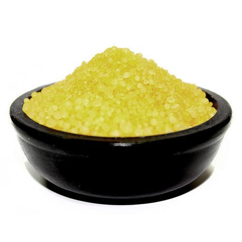 A yellow granular substance sits in a dark bowl. The substance is small, round and resembles coarse grains. The bowl is on a white surface.