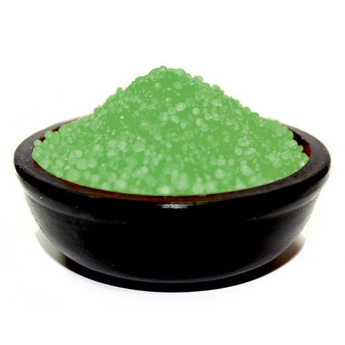 Green granules rest in a dark bowl. The granules appear to be a fine, granular substance. The bowl sits on a white surface.