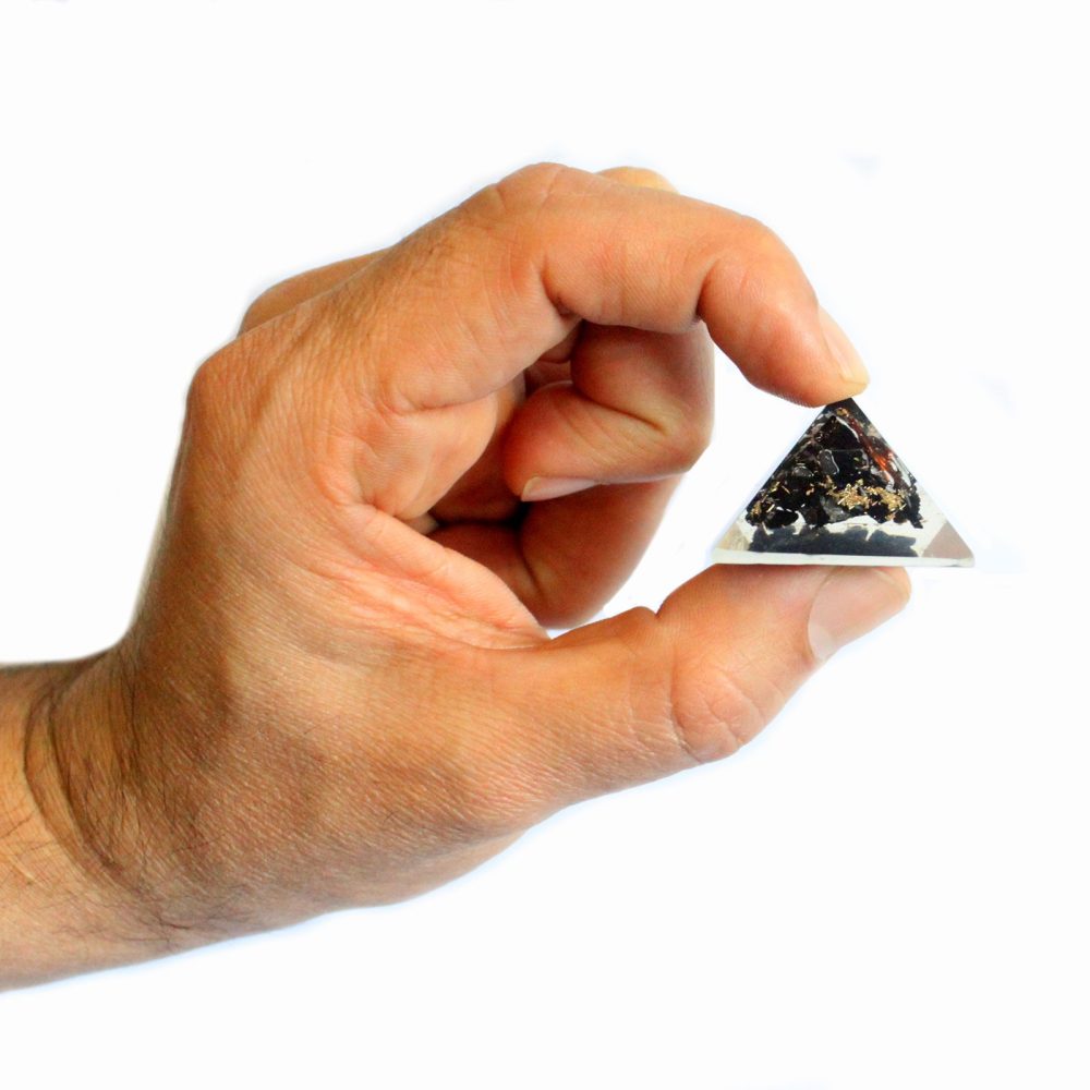 A hand holds a small, black, triangular crystal pyramid. The pyramid appears embedded in clear resin. The background is white.