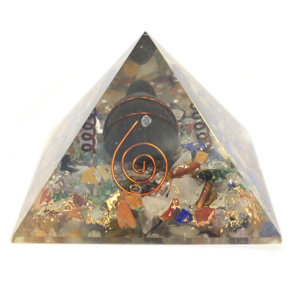 A crystal pyramid containing various colorful stones and a central dark orb, encased in clear resin, sits on a white surface.