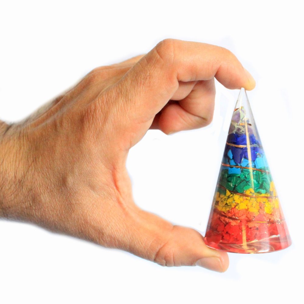 A hand holds a small, clear cone containing layered, multicolored stones; the cone is a rainbow of colors.