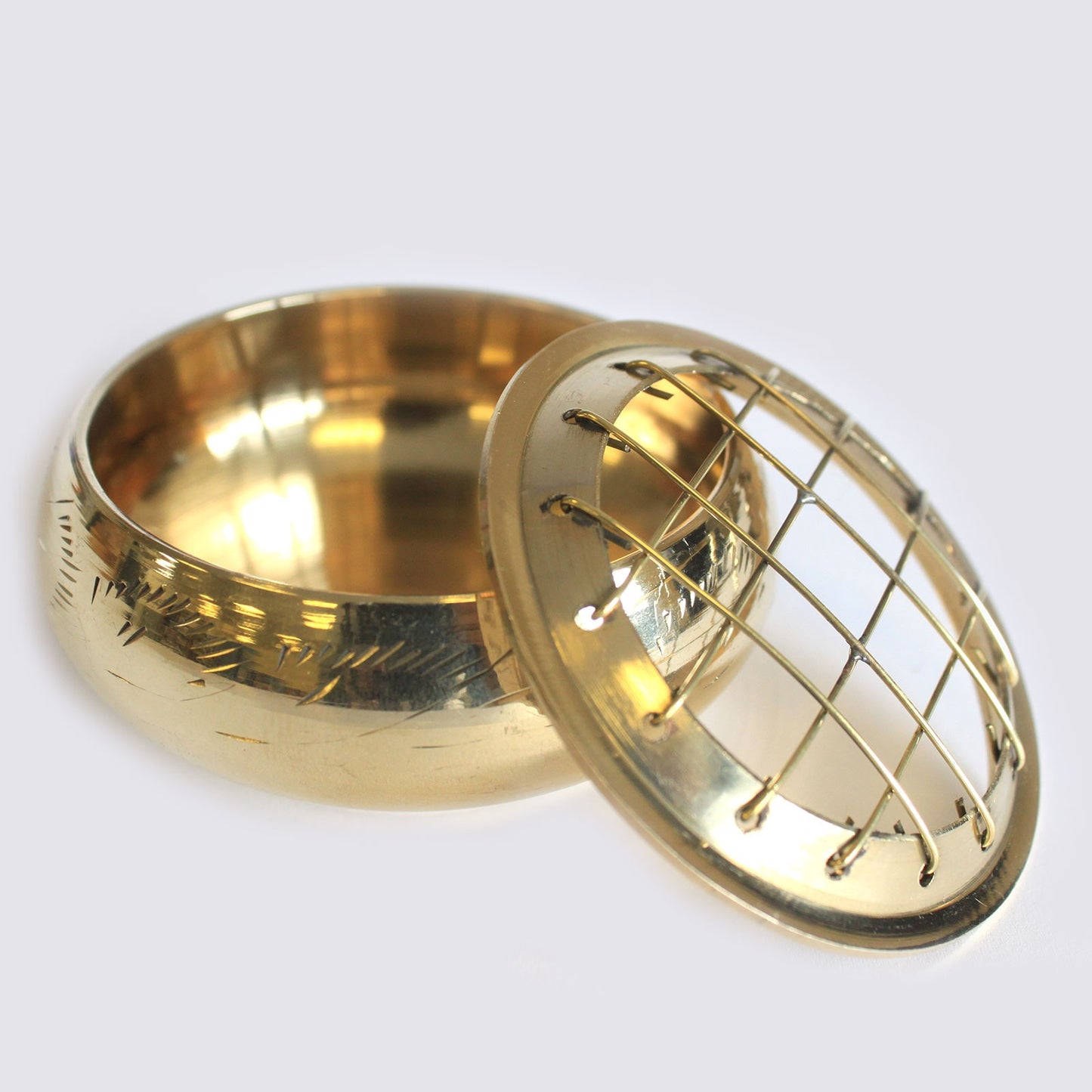 A brass pot with engraving rests open, featuring a removable lid with a grid design, on a plain, light background.