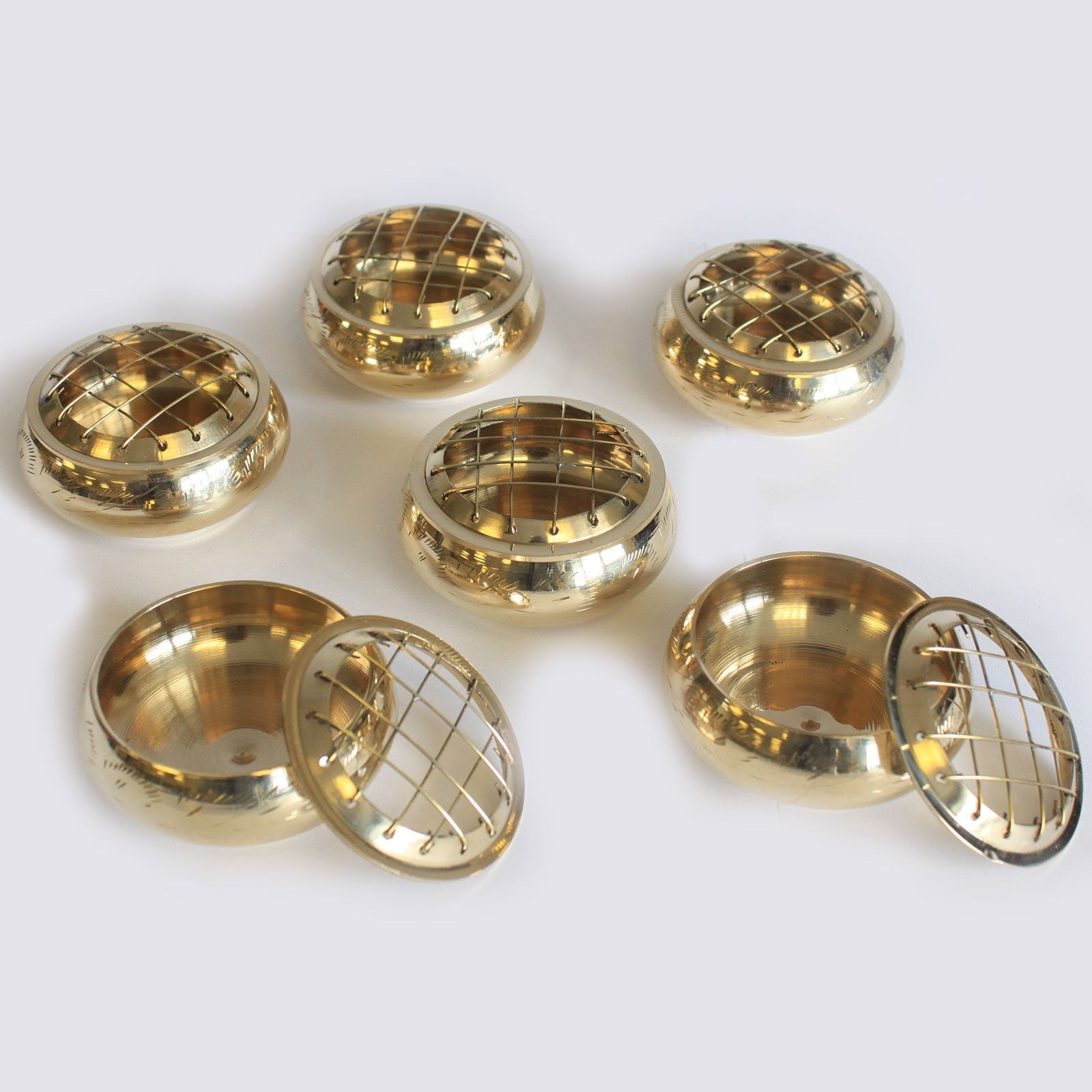 Six gold-colored, rounded brass containers with lattice-patterned lids lie scattered on a plain background. Two are open, displaying smooth interiors and the detachable lids nearby.