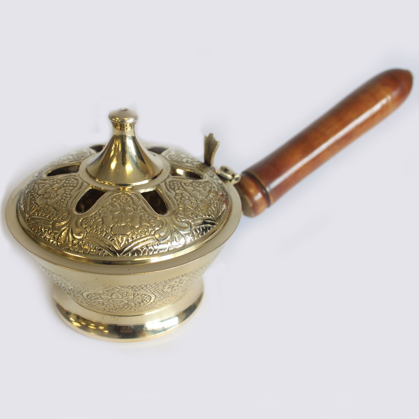 A detailed brass incense burner with floral engravings has a wooden handle, resting on a plain surface.