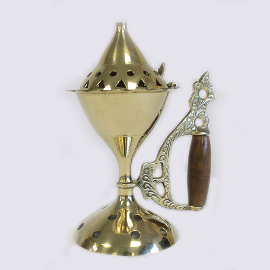 A brass incense burner, with a conical lid and perforated holes, stands upright. It features an ornate metal handle with a wooden grip, set against a plain background.