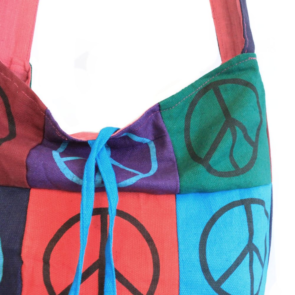 A fabric tote bag, with blue drawstrings, displays a patchwork of colorful squares, each with a printed peace sign. It is set against a white background.