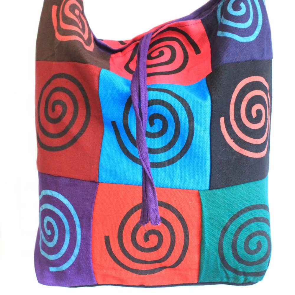 A colorful patchwork bag is displayed, each square featuring a painted spiral design. A violet drawstring cinches the top, against a bright white background.