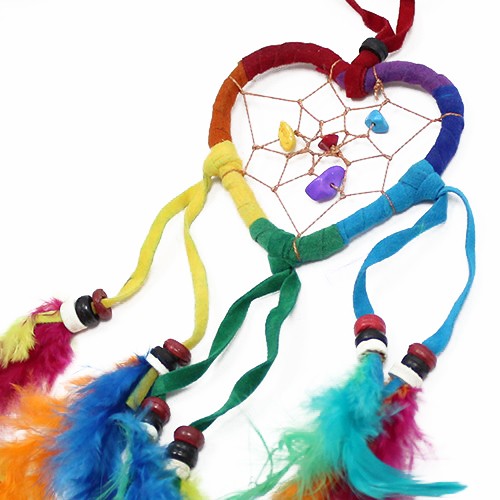 A heart-shaped dreamcatcher, adorned with colorful fabric, feathers, and beads, hangs against a white background.