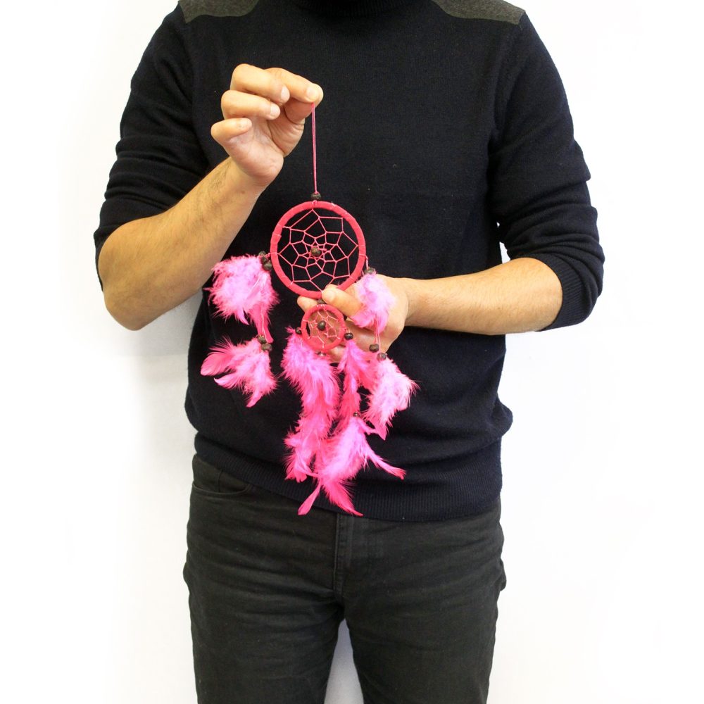 A person holds a pink dream catcher with feathers, against a white background.