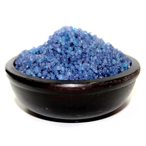 Blue granules rest in a dark bowl. The granules appear small and spherical. The bowl sits on a white surface.