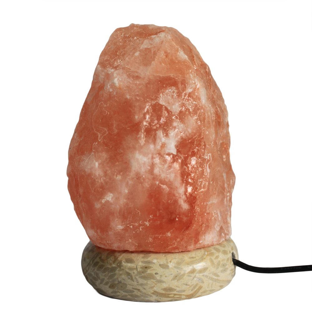 A pink Himalayan salt lamp rests atop a round, textured stone base, connected by a black power cord. The lamp has a rough, crystalline surface, providing a warm ambiance.
