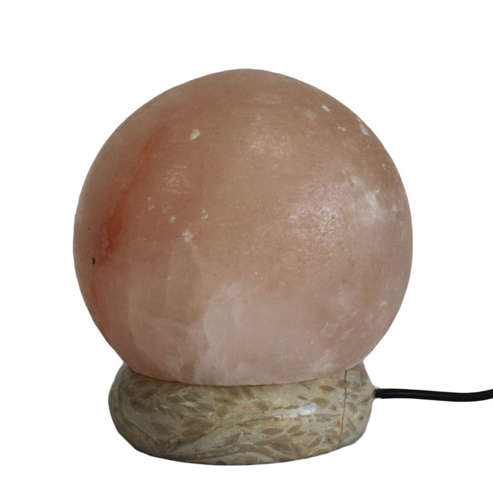 A spherical salt lamp rests on a carved stone base, connected by a black electrical cord. The lamp's surface is textured and variegated in shades of pink and white.