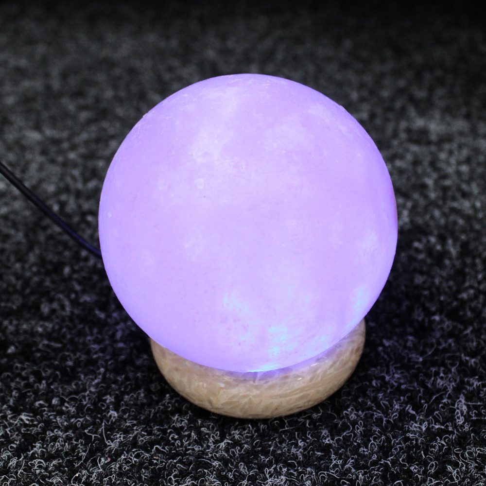 A glowing purple orb rests on a light-colored base, connected by a black cord, placed on a textured dark surface.