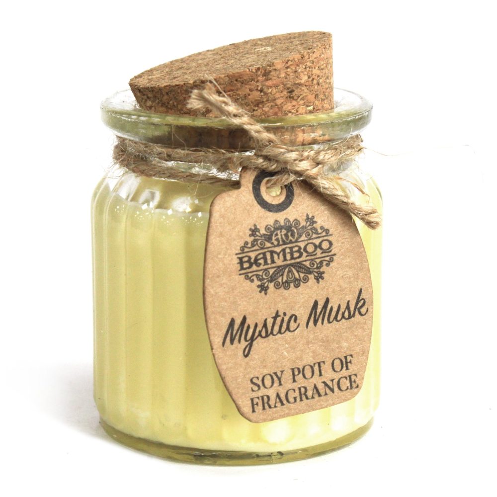 A glass jar with cork stopper and twine holds a pale yellow wax candle, labeled "BAMBOO Mystic Musk SOY POT OF FRAGRANCE," on a white surface.