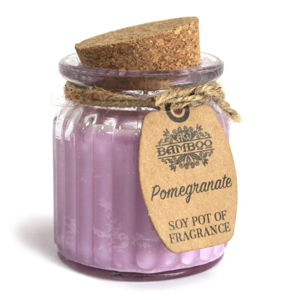 A purple candle rests in a clear, fluted jar, sealed with a cork stopper and twine; a brown tag reads "BAMBOO," "Pomegranate," and "SOY POT OF FRAGRANCE" against a white background.