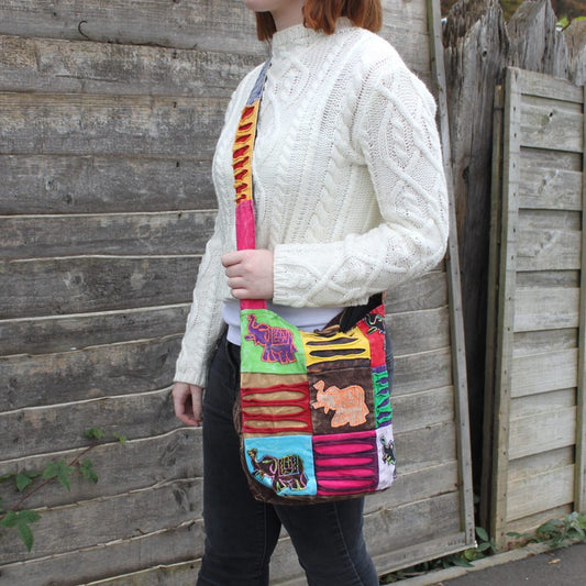 A woman carries a colorful patchwork elephant bag over her shoulder. The background is an old wooden fence.
