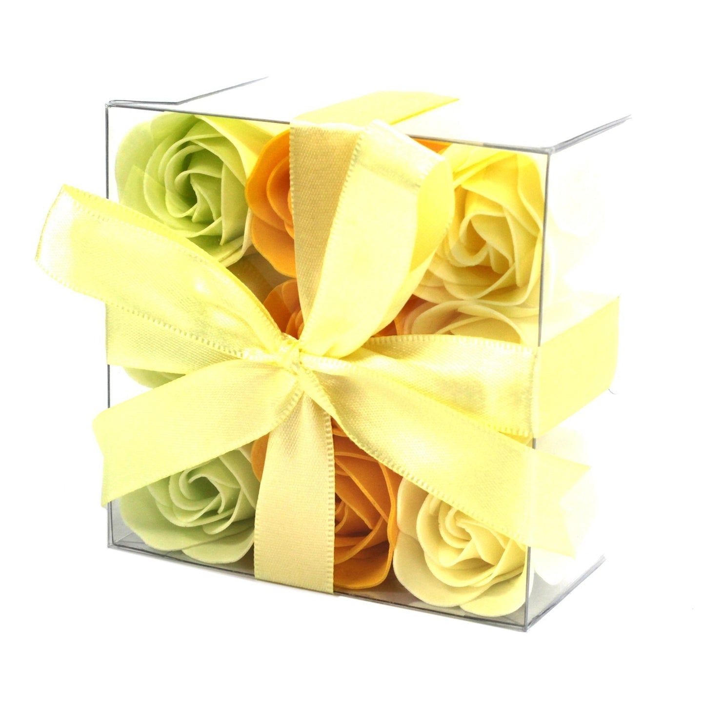 Rose-shaped soaps rest in a clear, cubic container. A yellow ribbon is tied in a bow around the box, which is isolated on a white background.