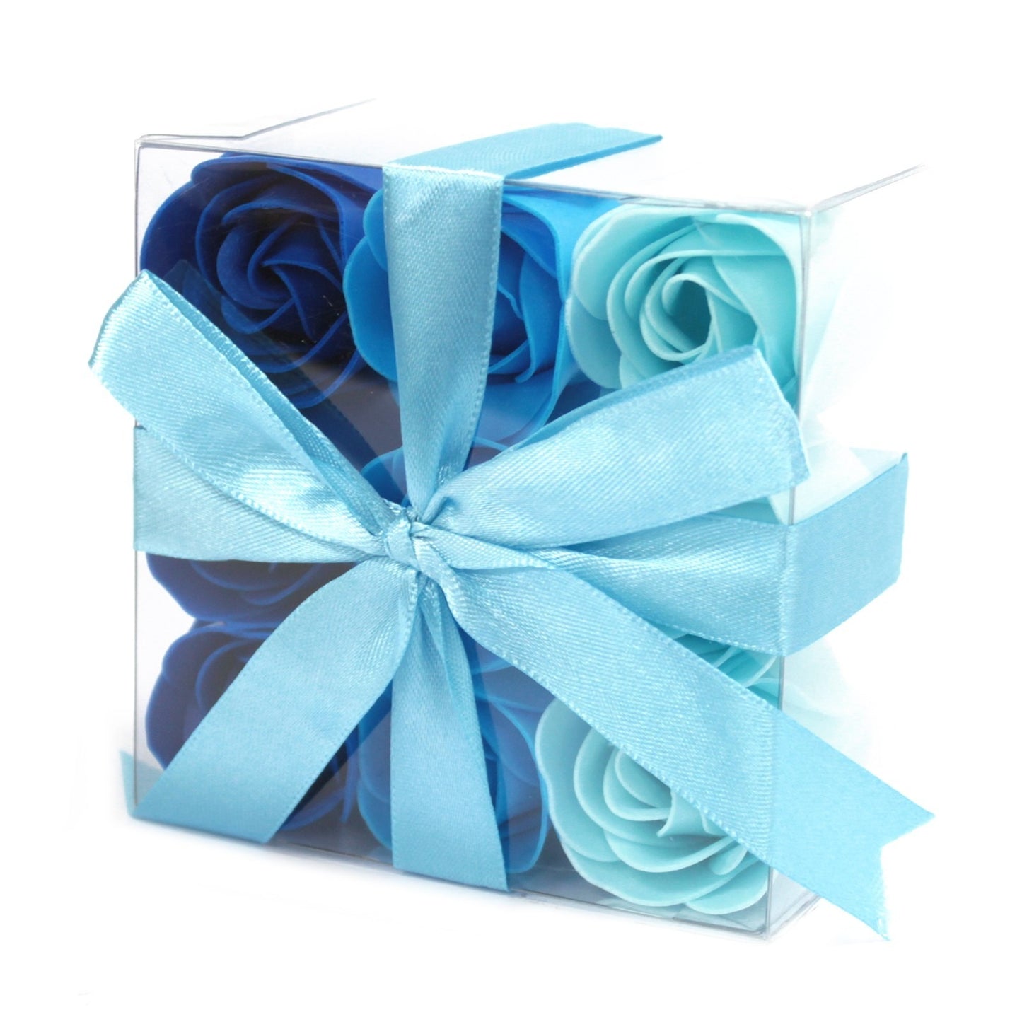 A clear, square box holds blue rose soaps, ranging from light to dark blue. A light blue satin ribbon wraps the box and is tied in a bow. The background is plain white.
