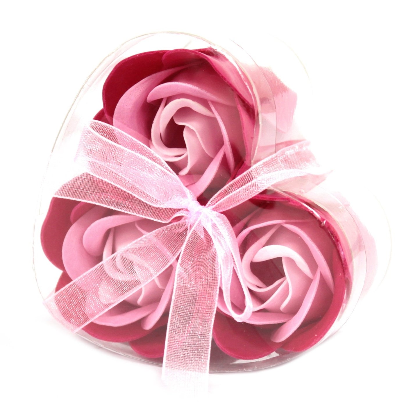 Three pink rose soaps rest inside a clear, heart-shaped container. A light pink ribbon is tied around the package. The backdrop is white.