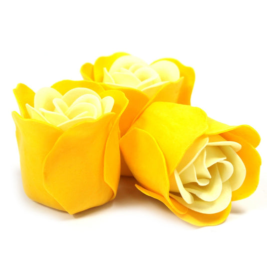 Three yellow rose-shaped soaps rest clustered on a white surface, their layered white centers and smooth petals shown in a close-up studio view.