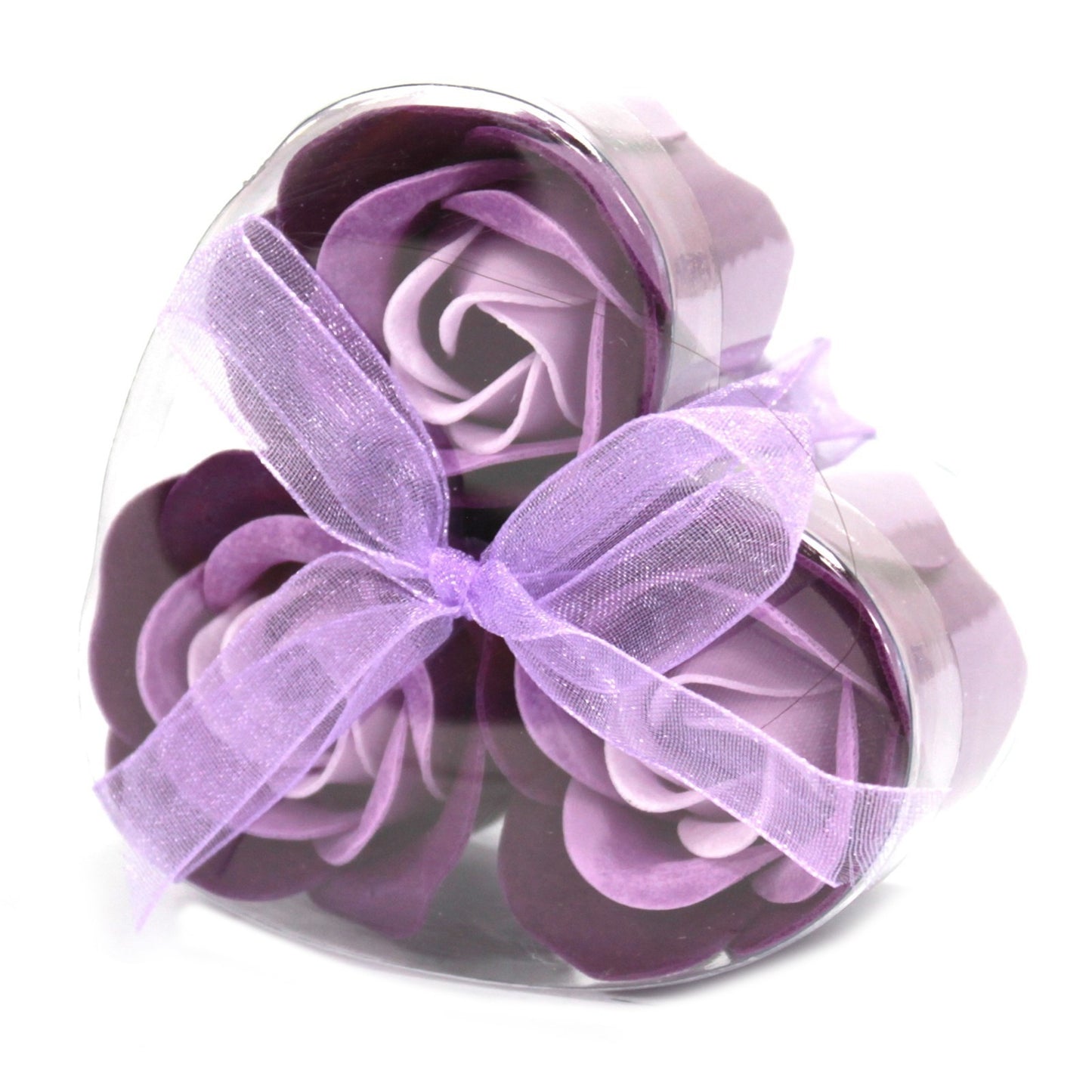 Three purple faux-rose soap flowers sit in a clear, heart-shaped box tied with a sheer, lavender bow, on a white background.