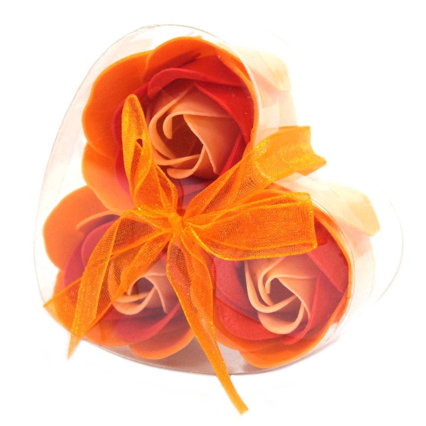 Soap roses rest in a clear, heart-shaped plastic container, secured with an orange ribbon bow. The roses are a blend of peach, orange, and red colors on a white background.