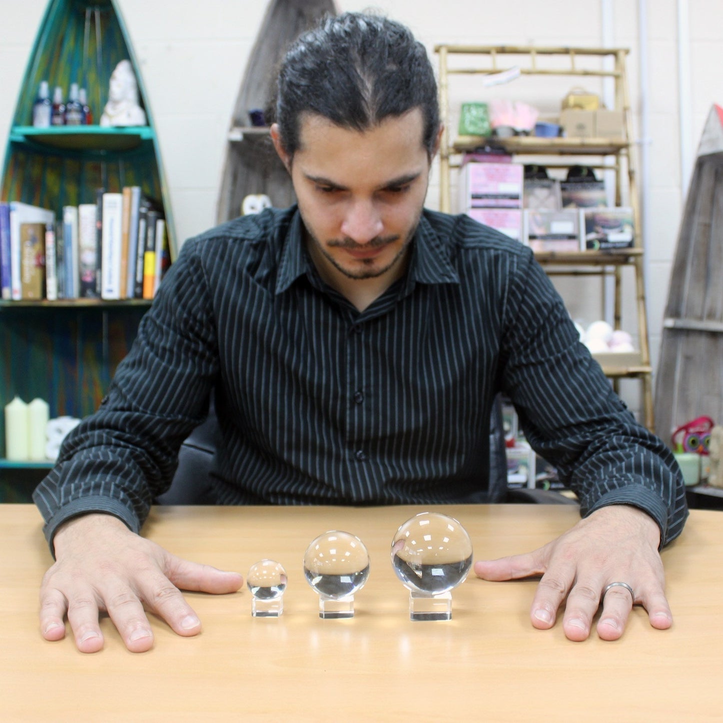A person gazes intently at three crystal spheres in varying sizes on a wooden table, surrounded by bookshelves displaying decor items in a cozy room.