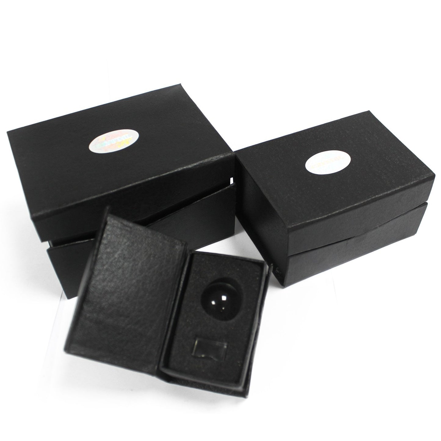 Black boxes with white oval labels are stacked; one box is open, displaying a black spherical object seated in a fitted cushion. The setting is plain and minimalistic.