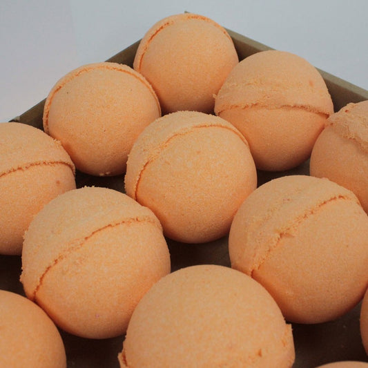 Round, orange bath bombs are neatly arranged in rows on a brown tray, creating a visually appealing pattern against a plain white background.