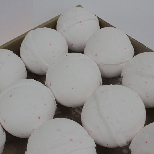 White spherical bath bombs rest in a cardboard box, each speckled with tiny pink dots, nestled closely together, ready for use in a relaxing bath setting.