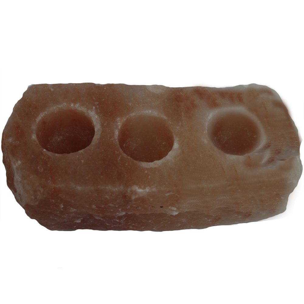 A rough-hewn, rectangular, pink salt block has three round, carved depressions to hold tea light candles, on a white background.