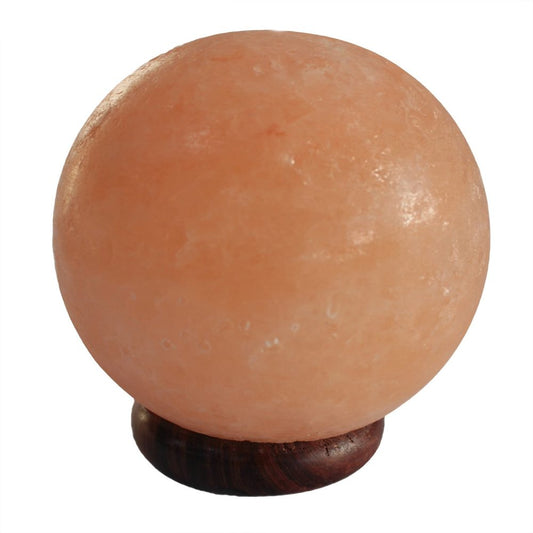 A round, pink Himalayan salt lamp rests on a small wooden base. The surface is slightly rough, reflecting light softly. It's placed against a plain white background.