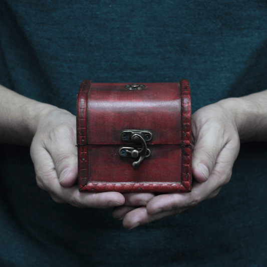 A small red wooden box with a metal latch is held in two hands. The person is wearing a dark shirt, providing a contrasting background.