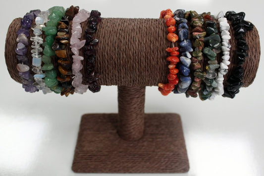 Chip bead bracelets are displayed on a brown jewelry stand, resting on a white surface. The bracelets feature a variety of colors and stones.