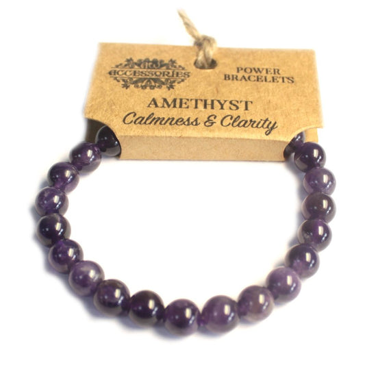 The purple Amethyst power bracelet loops, and the ends are attached to a small, brown tag. The tag reads, “Accessories,” “Power Bracelets,” and “Amethyst Calmness & Clarity.” The background is white.