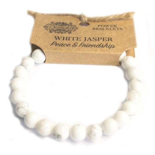 A white jasper bead bracelet sits against a kraft paper tag that reads "ACCESSORIES," "POWER BRACELETS," "WHITE JASPER Peace & Friendship," all on a white surface.