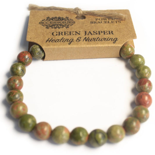 A Green Jasper bracelet sits with a craft tag that reads "ACCESSORIES POWER BRACELETS GREEN JASPER Healing & Nurturing" against a white backdrop.